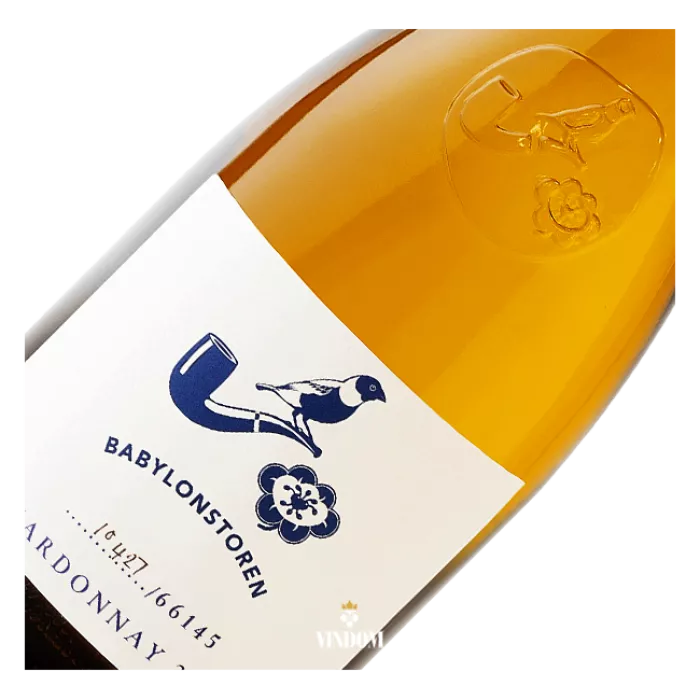 Babylonstoren Chardonnay 2025, Simonsberg-Paarl Babylonstoren Chardonnay 2025 is een rijke, verfijnde witte wijn van 100% Chardonnay uit Simonsberg-Paarl in Zuid-Afrika. Romige citrus en groene appel combineren met meidoornbloesem, jasmijn, fijne houtkruiden en een frisse minerale spanning. De wijn vergist deels op 300-liter Frans eiken en rijpt in totaal tien maanden, met 35% nieuw hout. Toch blijft hij levendig en precies. De jaargang 2025 kreeg 92 punten bij de Investec Trophy Wine Show 2026, Double Gold bij de National Wine Challenge en zilver bij Chardonnay du Monde 2026.  Hoe smaakt Babylonstoren Chardonnay 2025? De kleur is lichtend goud met zilveren schakeringen, helder en geconcentreerd. In de geur openen florale aroma’s van meidoornbloesem en jasmijn. Daarna volgen citroengras en knapperige groene appel, met fijne houtkruiden als subtiele achtergrond.  In de mond is de wijn droog, vol en zijdeachtig. Romige citrus geeft volume, terwijl levendige zuren en mineraliteit voor spanning en precisie zorgen. Het Franse eiken voegt een zachte kruidigheid toe zonder het fruit te overheersen. De afdronk is lang, fris en gelaagd.  Waarom blijft deze houtgerijpte Chardonnay zo precies? Babylonstoren zoekt bij deze Chardonnay niet alleen naar rijkdom. De kracht zit juist in het samenspel tussen romigheid, frisse zuren en beheerste houtinvloed. Daardoor krijgt de wijn voldoende volume en structuur zonder zwaar te worden.  Ook de keuze van de vaten speelt daarin een belangrijke rol. De wijn gebruikt 35% nieuw Frans eiken en 65% tweedejaars vaten. Nieuw hout brengt meer kruidigheid en structuur, terwijl gebruikte vaten het fruit meer ruimte geven. Dat levert een stijl op die liefhebbers van Bourgondisch geïnspireerde Chardonnay zal aanspreken: rijk en verfijnd, maar met voldoende frisheid en mineraliteit om de wijn scherp omlijnd te houden.  Chardonnay van de hellingen van de Simonsberg De druiven komen van de hellingen van de Simonsberg, tussen Franschhoek, Stellenbosch en Paarl. Het officiële herkomstgebied voor deze wijn is Simonsberg-Paarl, binnen de Western Cape van Zuid-Afrika.  Babylonstoren gebruikt voor deze wijn uitsluitend Chardonnay. De druif levert hier voldoende rijpheid en concentratie voor vatrijping, terwijl frisse zuren de wijn spanning geven. Daardoor kunnen fruit, lie en Frans eiken zich ontwikkelen zonder dat één element de stijl volledig bepaalt.  Van hele trossen naar 300-liter Frans eiken De druiven worden als hele trossen geperst. De vergisting begint in roestvrijstalen tanks, zodat het verse fruitkarakter aanvankelijk centraal blijft staan. Op de derde dag verhuist de fermenterende wijn naar Franse eikenhouten vaten van 300 liter.  Van deze vaten is 35% nieuw en 65% tweedejaars. Die combinatie geeft Babylonstoren meer controle over de houtinvloed. Het nieuwe eiken voegt structuur en kruidigheid toe, terwijl de gebruikte vaten de Chardonnay vooral ruimte geven om zich verder te ontwikkelen.  Wat doen lie-rijping en bâtonnage met de wijn? Na de fermentatie blijft Babylonstoren Chardonnay drie tot vier maanden op de primaire lie. Tijdens deze periode vindt iedere twee weken bâtonnage plaats, waarbij het bezinksel van fijne gistcellen opnieuw door de wijn wordt geroerd.  Dat draagt bij aan de romige en zijdeachtige textuur. Daarna wordt de wijn overgestoken en rijpt hij nog zes maanden verder op vat. In totaal krijgt Babylonstoren Chardonnay 2025 tien maanden rijping vóór de botteling.  Juist deze combinatie verklaart veel van het karakter van de wijn. Lie-rijping geeft volume en zachtheid, Frans eiken brengt structuur en kruidigheid, terwijl de natuurlijke frisheid van de Chardonnay het geheel in balans houdt.  92 punten, Double Gold en internationaal zilver Babylonstoren Chardonnay 2025 kreeg bij de Investec Trophy Wine Show 2026 92/100 punten en een zilveren medaille. De competitie vermeldt de wijn specifiek als 100% Chardonnay uit Simonsberg-Paarl in de categorie houtgerijpte Chardonnay.  Daar bleef het niet bij. De National Wine Challenge 2026 bekroonde dezelfde jaargang met Double Gold. Ook internationaal kreeg de wijn erkenning: bij Chardonnay du Monde 2026 behaalde Babylonstoren Chardonnay 2025 een zilveren medaille.  Die drie onderscheidingen geven samen een sterk beeld van jaargang 2025: een houtgerijpte Chardonnay met voldoende concentratie voor rijkdom, maar ook de frisheid en precisie om zijn balans te behouden.  Babylonstoren aan de voet van de Simonsberg Babylonstoren is een historisch Kaaps landgoed aan de voet van de Simonsberg. Het domein combineert zijn agrarische geschiedenis met moderne wijnbouw, gastronomie en een sterke aandacht voor de relatie tussen landschap en product.  De wijnproductie onder het Babylonstoren-label begon met de oogst van 2011. Keldermeester Charl Coetzee en wijnmaker Klaas Stoffberg ontwikkelden sindsdien een herkenbare stijl waarin rijp Zuid-Afrikaans fruit samengaat met beheerste vinificatie, structuur en frisheid.  Deze Chardonnay past daar uitstekend bij. De wijn heeft duidelijk de rijkdom van vatrijping en lie-contact, maar behoudt genoeg zuur en minerale spanning om verfijnd te blijven.  Wat eet je bij Babylonstoren Chardonnay 2025? De combinatie van romige textuur, citrus, frisse zuren en Frans eiken maakt deze Chardonnay bijzonder geschikt voor rijke visgerechten. Denk aan gebakken of geroosterde vis, romige pasta en risotto met paddenstoelen.  Ook kalfsvlees met een romige saus sluit mooi aan. Klassieke sauzen als beurre blanc, hollandaise en béarnaise vinden aansluiting bij de volle textuur, terwijl de zuren van de wijn voldoende tegenwicht geven aan boter en room.  Serveer Babylonstoren Chardonnay 2025 licht gekoeld rond 11–12 °C. Zo blijven citrus, florale aroma’s en frisheid helder, terwijl de romige structuur en fijne houtkruiden voldoende tot hun recht komen.  Meer Babylonstoren ontdekken De Chardonnay laat de rijke, houtgerijpte witte stijl van Babylonstoren zien, maar het domein heeft een veel breder profiel. De Babylonstoren Babel vertegenwoordigt de toegankelijke rode blendstijl, terwijl Babylonstoren Nebukadnesar meer concentratie en kracht laat zien.  Voor mousserende wijn is er de Babylonstoren Sprankel MCC. Samen laten deze wijnen zien hoe Babylonstoren verschillende stijlen vanuit hetzelfde Zuid-Afrikaanse domein benadert.